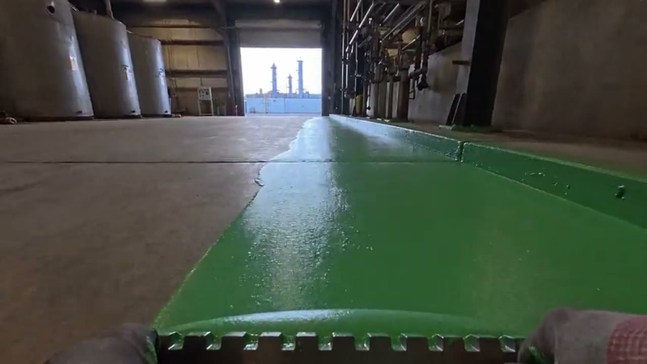 A squeegee spreading green coating across a plant floor